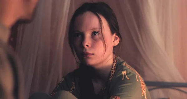 A still from the film What Marielle Knows. A white girl around 12 years of age, wearing giraffe pyjamas, with an unimpressed expression.