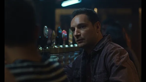 A still from the film Too Many Beasts. A white man hanging out at a bar looks over the white man beside him.