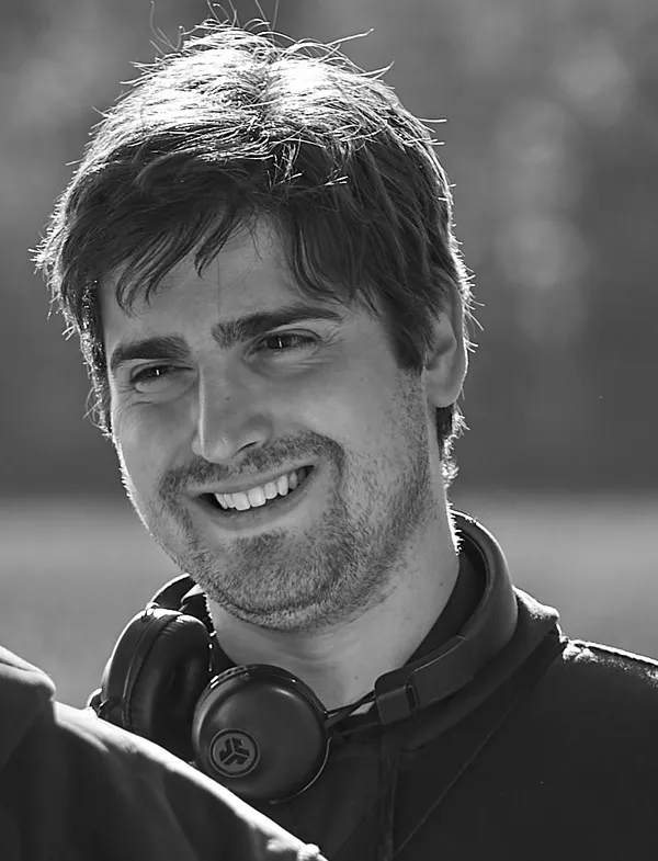 The filmmaker Mark H Rapaport, in black and white. A smiling white man with prominent stubble and headphones round his neck.