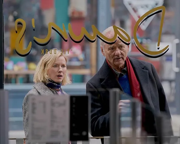 A still from the film The Friend.  A blond white woman and an older white man peer through the window of a shop from the street.