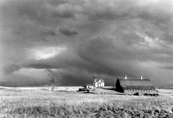 A still from the film Northern Lights. A barn and, behind it, a house, both low down in the frame, on a wide prairie beneath a huge, cloudy sky.