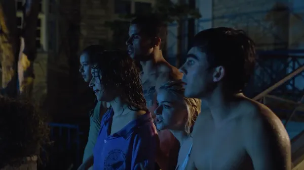 A still from the film Pools. A group of scantily-clad young people stand in a row outside a large house at night.