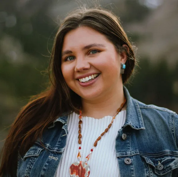 The filmmaker Paige Bethmann. A smiling Haudenosaunee woman wearing a white top and a denim jacket.