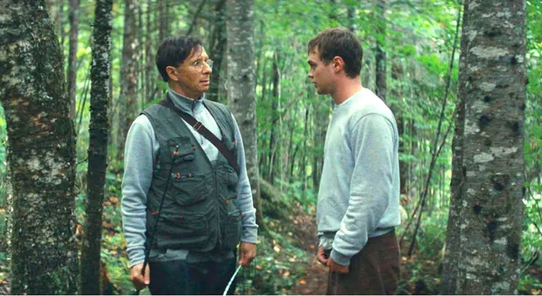 A still from the film Who By Fire. Two men stand facing one another in woodland.