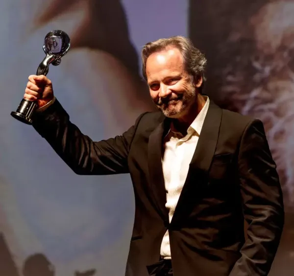 Peter Sarsgaard holding his President's Award in the air