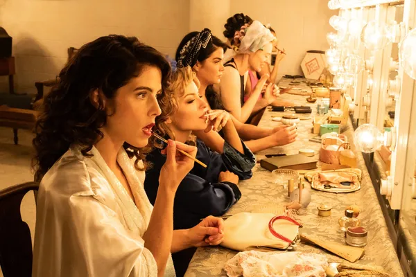 A still from the film Queen Of The Ring. White women sit in a row at a backstage dressing room, doing their make-up.