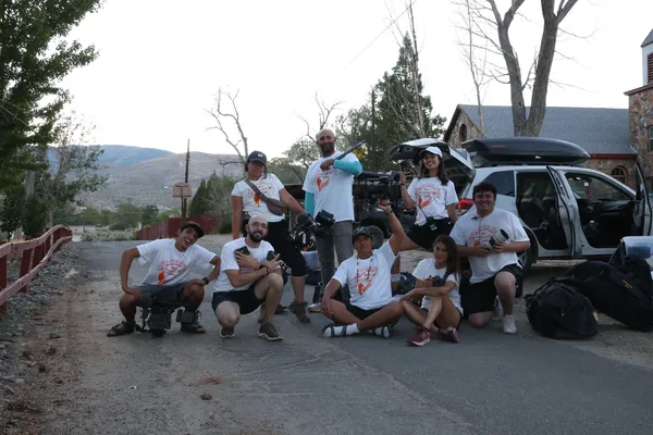 A behind the scenes shot from the film Remaining Native. Eight members of a film crew pose on a narrow village road, with bags stacked up beside them and hills in the distance.