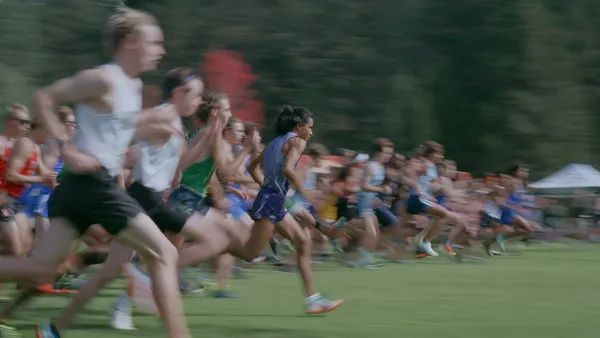A still from the film Remaining Native. A group of athles sprint across a field, with tell trees in the background.