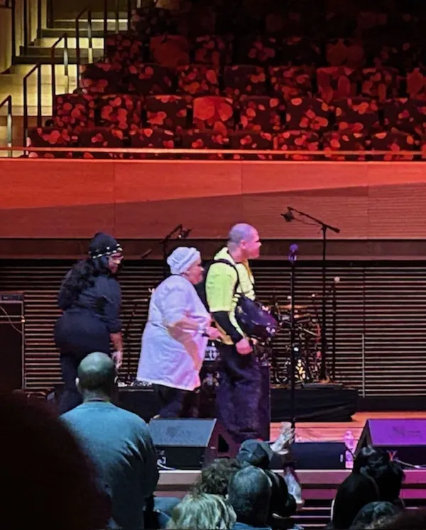 Three people stand on a stage in a crowded auditorium.