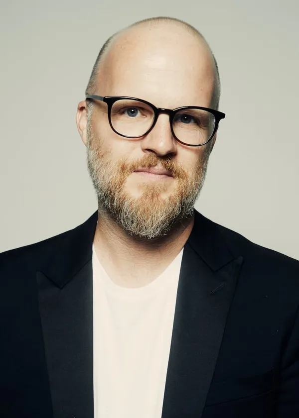 The filmmaker Rod Blackhurst. A white man with minimal head hair, a short, neat beard and black-framed glasses.
