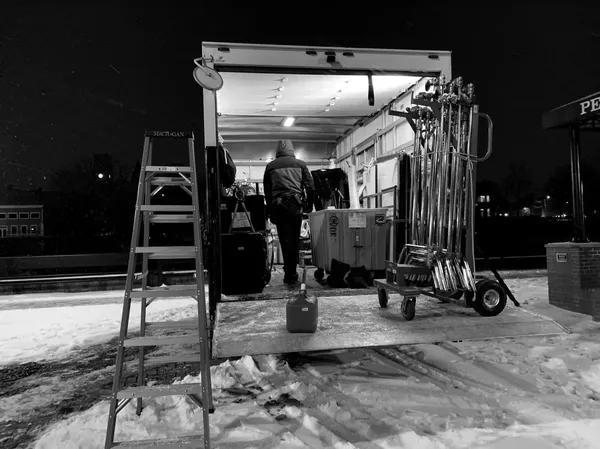 A behind the scenes shot from the film Stationed At Home. On a snowy night, filmmaking gear is being unloaded from the back of a truck onto an icy street.