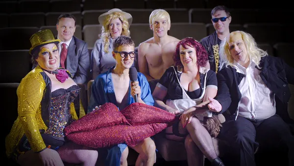 A still from the film Sane Inside Insanity: The Phenomenon Of Rocky Horror. A group of white people in Rocky Horror costumes sit together in cinema seats, holding a giant pair of lips.