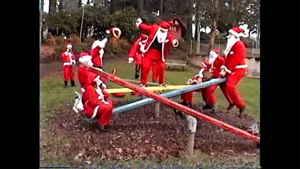A still from the film Santacon. A group of people dressed as Santa play on seesaws in a park.