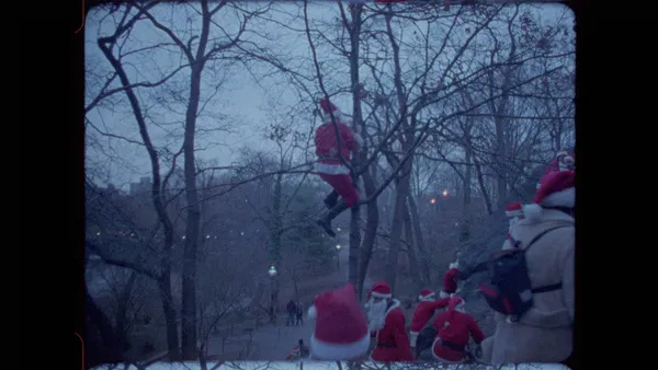 A still from the film Santacon. Several people dressed as Santa climb a leafless tree.