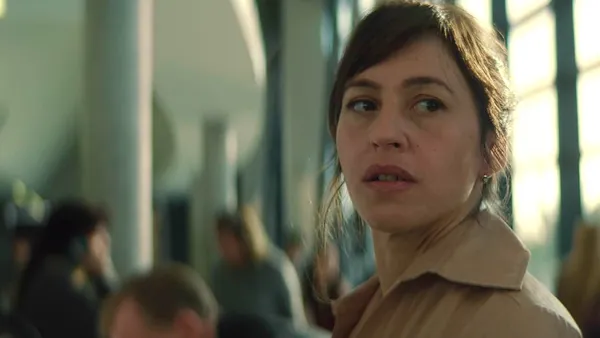 A still from the film Dead Language. A white woman looks around an airport nervously.
