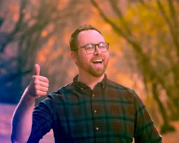 The filmmaker Simon Glassman. An unnaturally cheerful white man walking through Autumn foliage and making a thumb's up gesture.