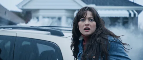 A still from the film This Is Not A Test. A young white woman stands beside a car on a chilly day, looking shocked.