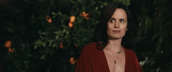A still from the film The Uninvited. A white women with long dark hair, wearing a red evening dress, stands in an orange grove at night.