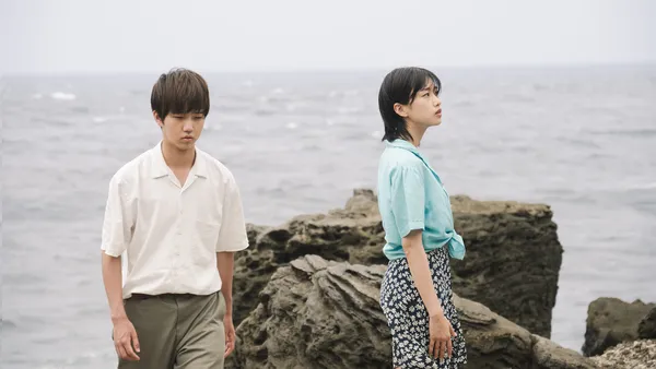 A young man and a woman look in different directions by the sea