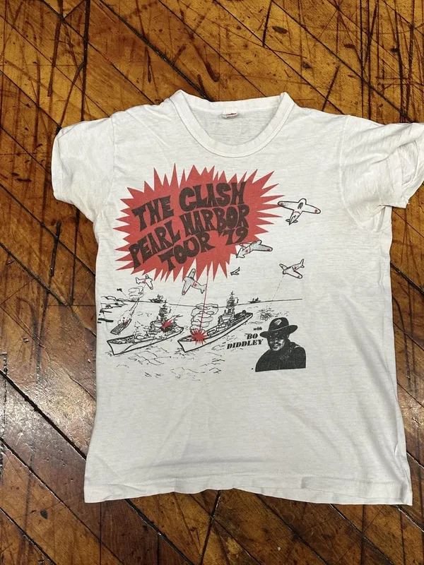 A T-shirt featuring an image of small aeroplanes firing at large ships, with the words 'The Clash Pearl Harbor Tour '79, with Bo Diddley.'