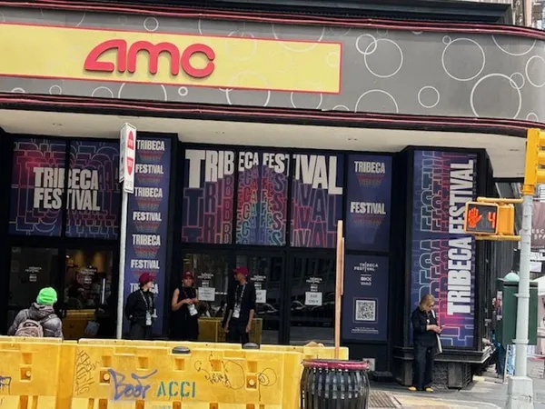 A corner building in an urban area, with the stylised letters 'AMC' on a yellow sign above it. Its windows are plastered with materials advertising the Tribeca Film Festival.