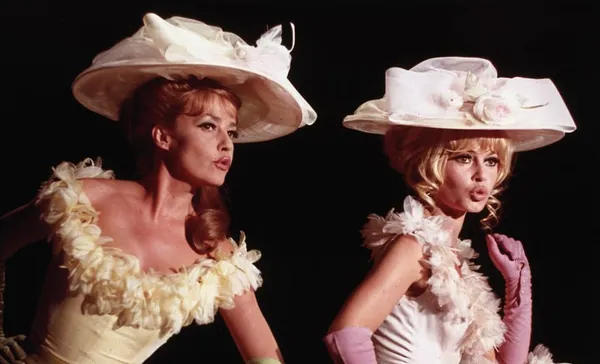 A still from the film Viva Maria. Two pouting white women wearing feather-trimmed bodices and elaborate hats.