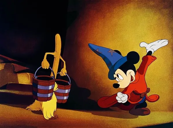 A still from the animated film Fantasia. Mickey Mouse, wearing wizarding robes, gestures to a broom-based creature which is walking along carrying two full buckets.