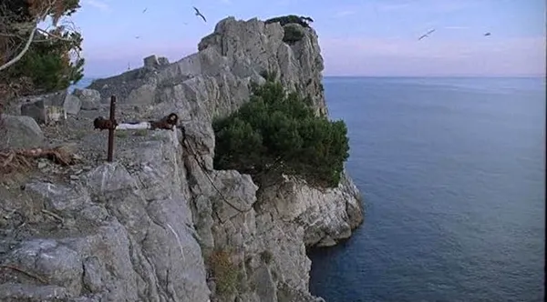 A still from the film Weightless. A rocky promontory with a tree clinging to one side of it stretches out into the sea.