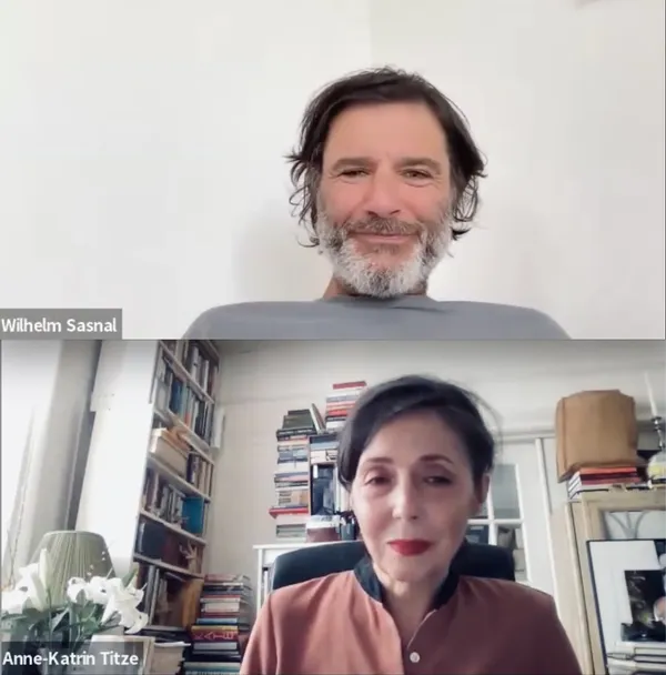 A middle-aged white man with dark hair and a mostly white beard sits against a plain white wall in one Zoom window; in another, a middle-aged, brown-haired white woman is surrounded by books.