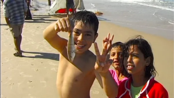 A child is on a beach holding a fish towards the camera
