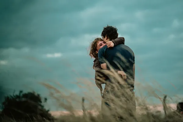 A still from the film Urchin. Two white people embrace in a field, lightly touched by firelight.
