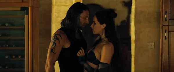 A still from the film Compulsion. A white woman in skimpy black clothing and a long-haired, a tattooed white man get close in a wine cellar.