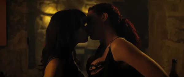 A still from the film Compulsion. A dark-haired young white woman and a red-haired white woman kiss in an indoor space with exposed stone walls.