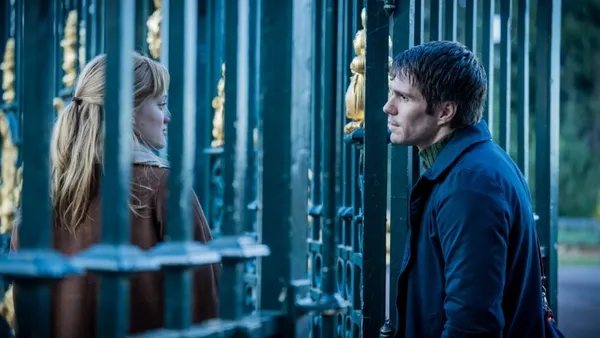 A woman and a man look at one another through a fence
