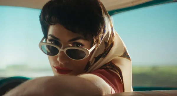 A woman peers over sunglasses while looking over her shoulder