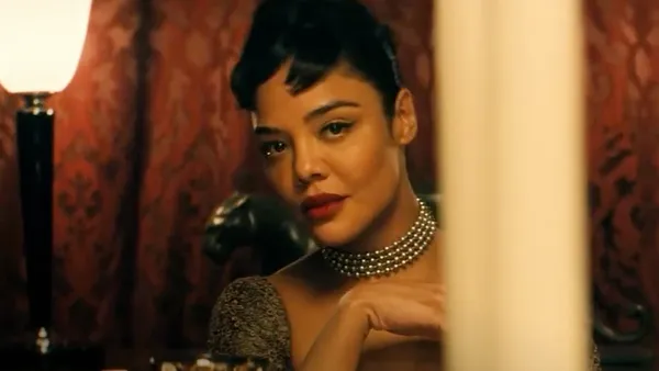 A still from the film Hedda. A young Black woman in glamorous 1950s clothing peers out from behind a pillar.
