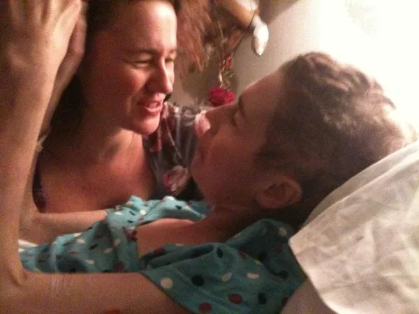 Twin white women in their early forties talk in a hospice, one of them lying on a bed.