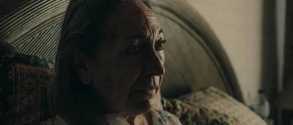 A still from the film Paris 70. An elderly white woman sits in bed, looking slightly bewildered.
