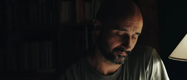 A still from the film Paris 70.  A white man sits in front of a bookcase, in shadow.