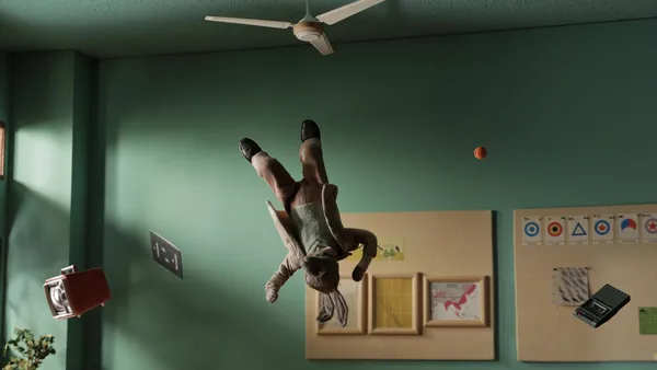 A still from the film Tennis, Oranges. An elderly male rabbit performs a martial arts move, somersaulting through a room with turquoise walls, alongside an orange.