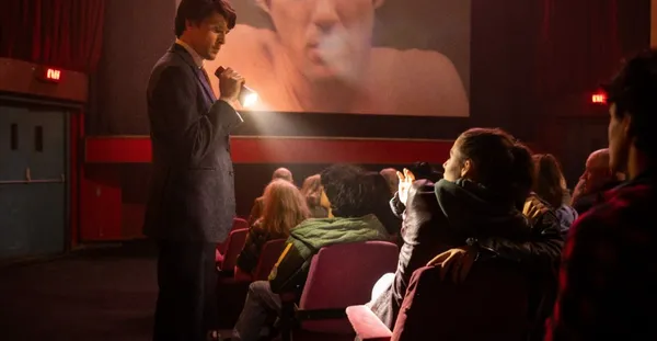 A cinema usher shines a torch at a seated woman as a film plays